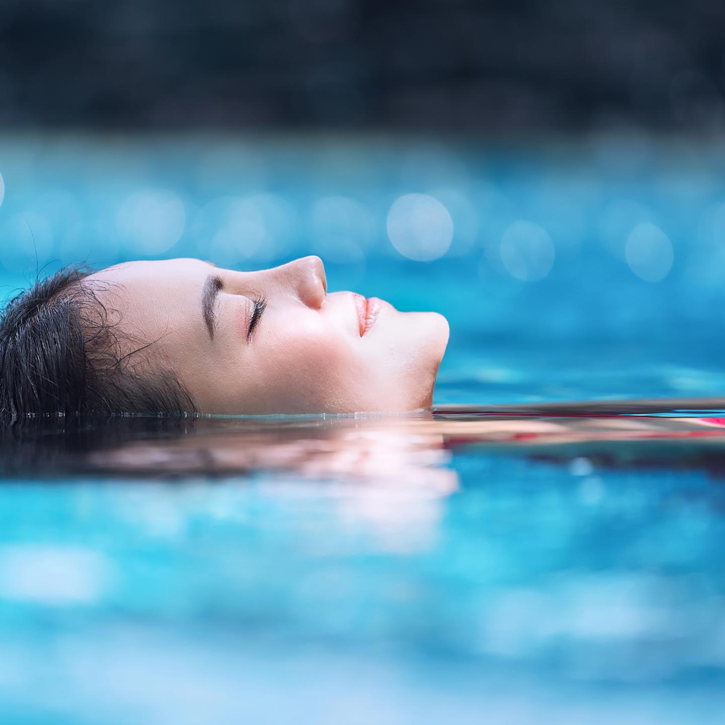 Person in a swimming pool, their head is resting in the water and their eyes are closed