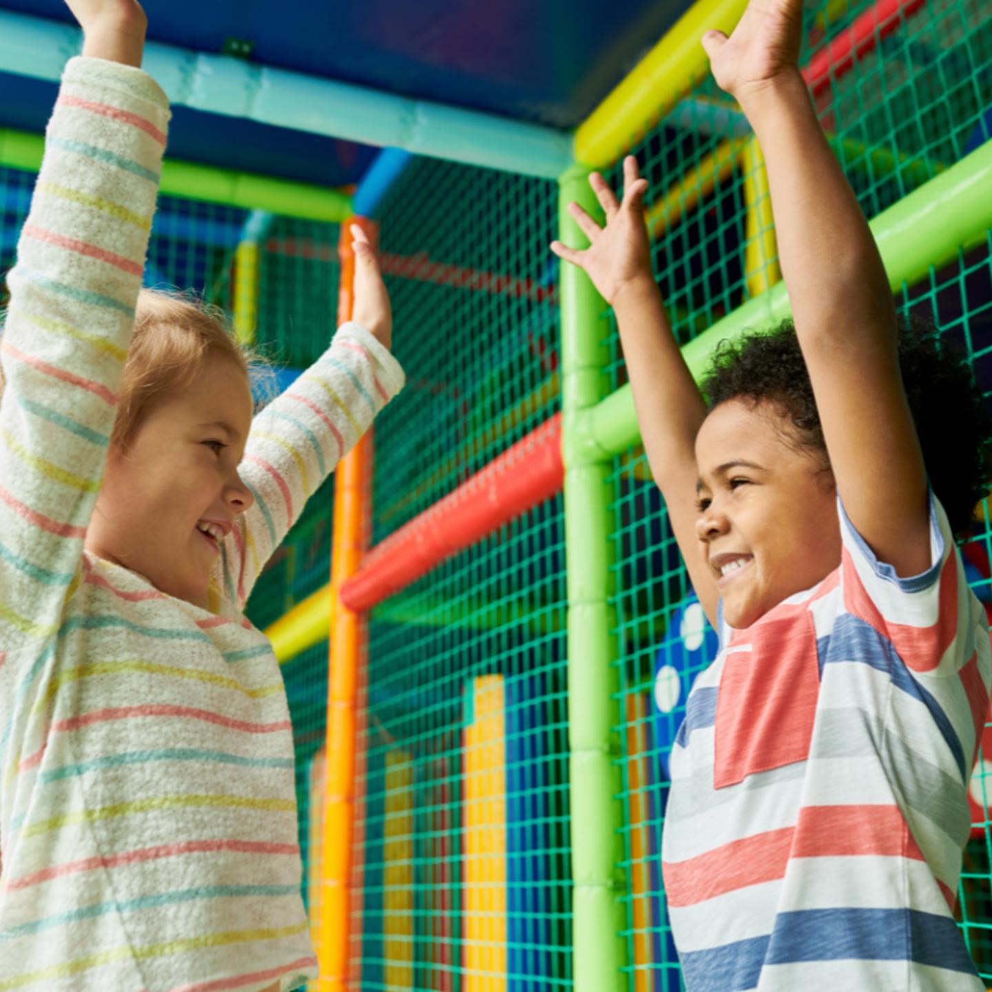 Photo of two excited children looking at each other with their hands in the air in the Playzone area