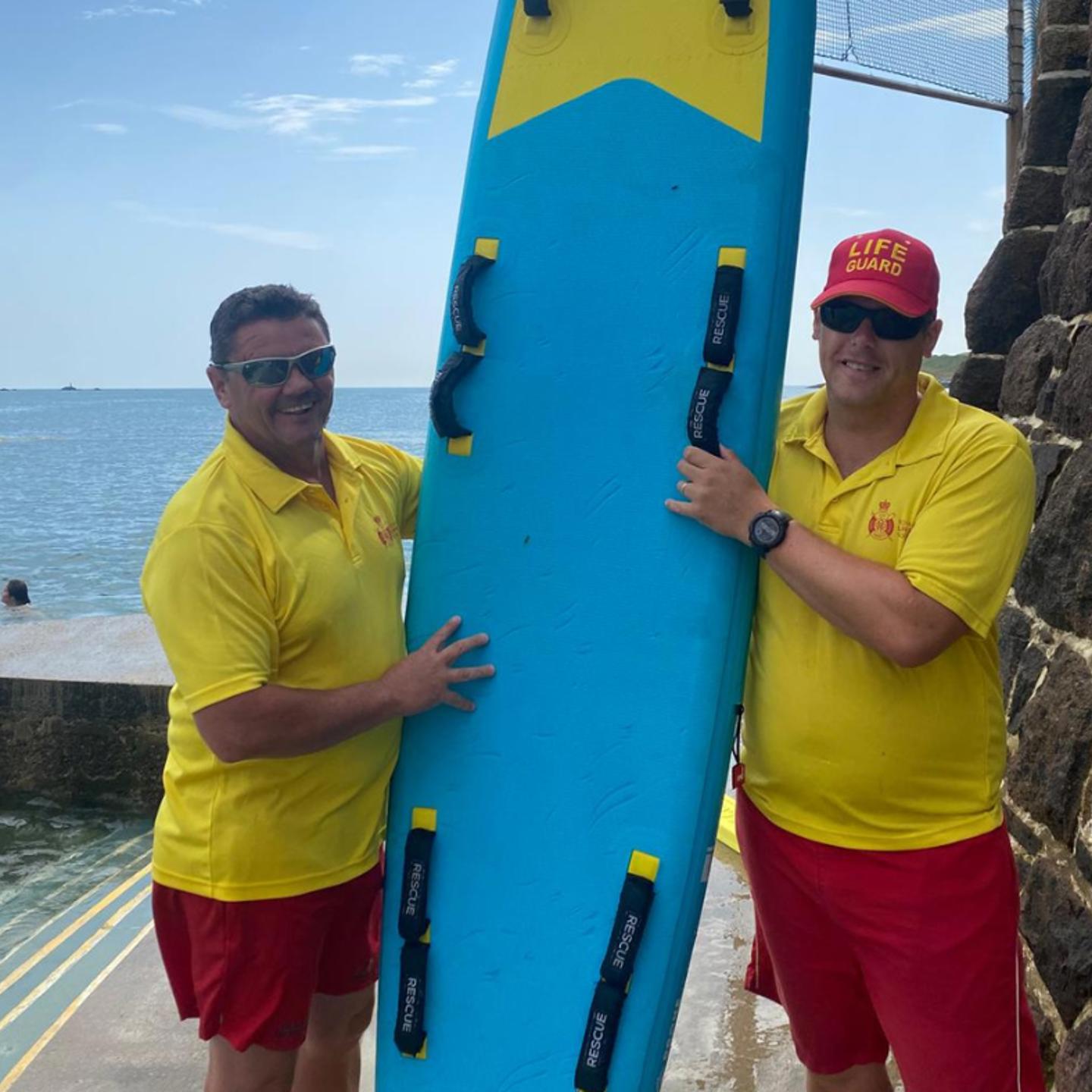 Photo of two of the lifeguards at the Havre Des Pas Bathing Pool holding a rescue board between them