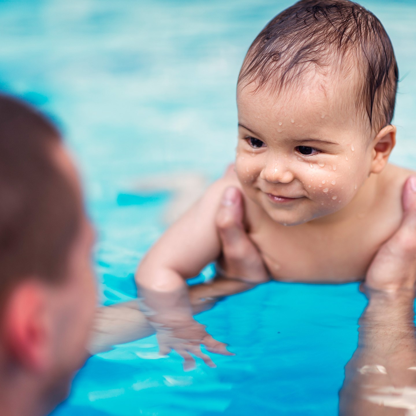 Adult holding baby that is learning to swim with water on it's face