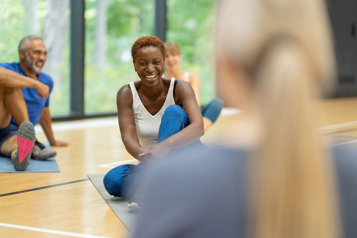 Group of people sitting on matts on the floor, person in the centre of the photo is smiling