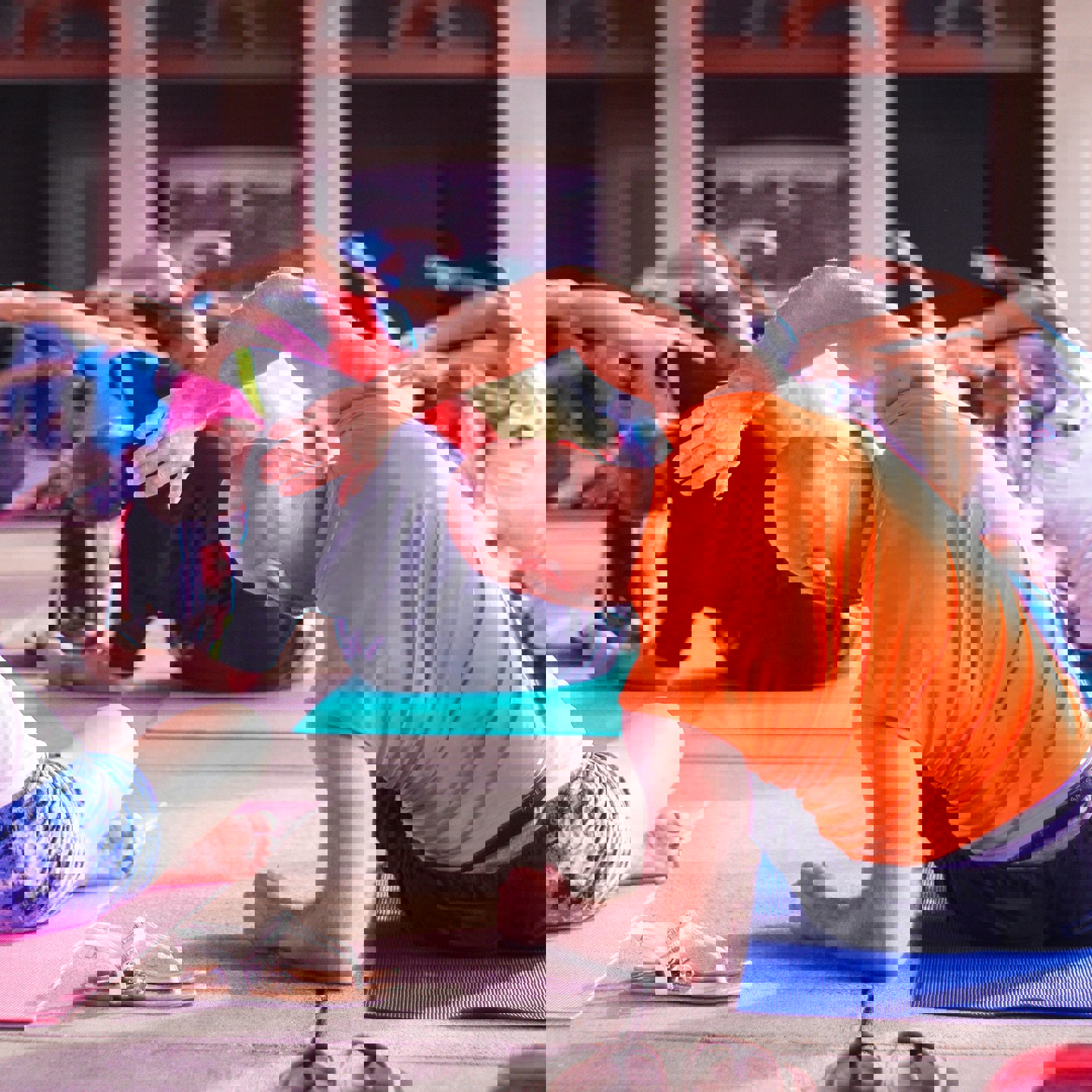 Photo of people on the floor stretching as part of a class, the photo is taken from behind so you can only see the backs of people