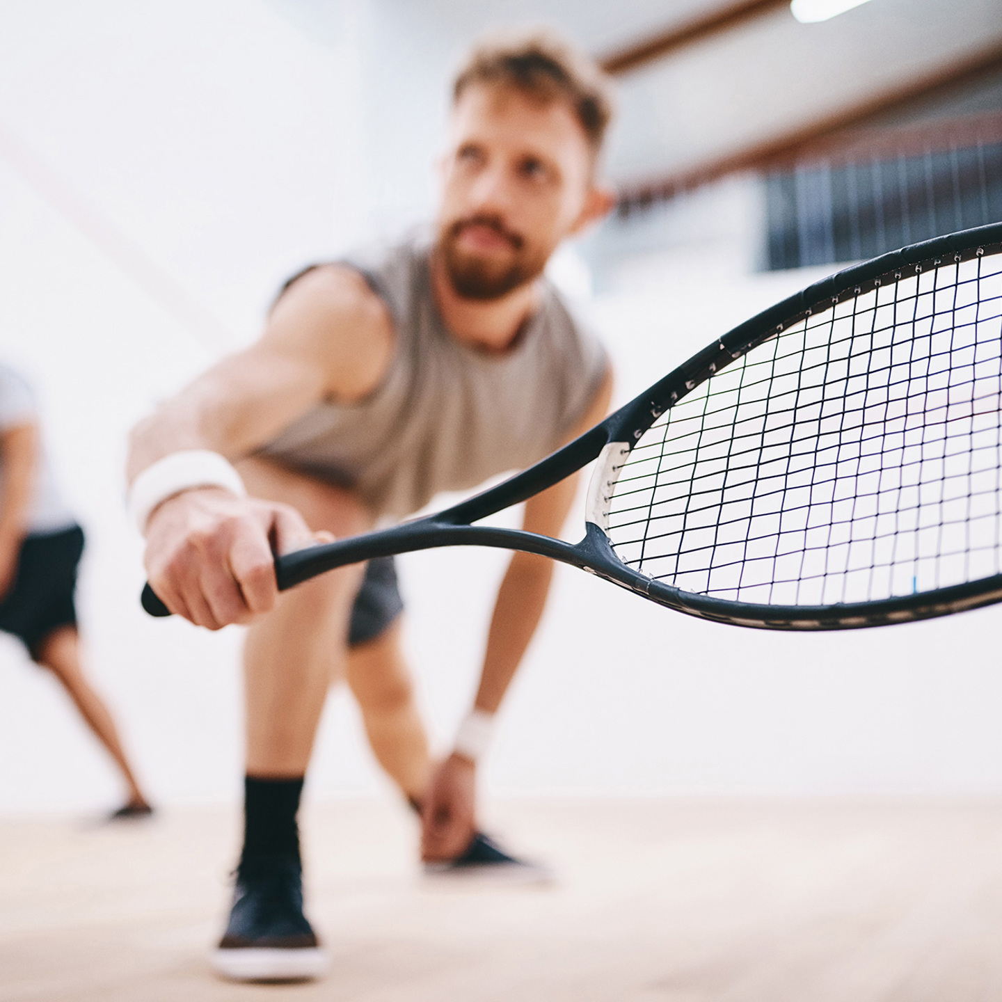 Man playing squash with the racquet near the camera, blurry person behind them playing as well