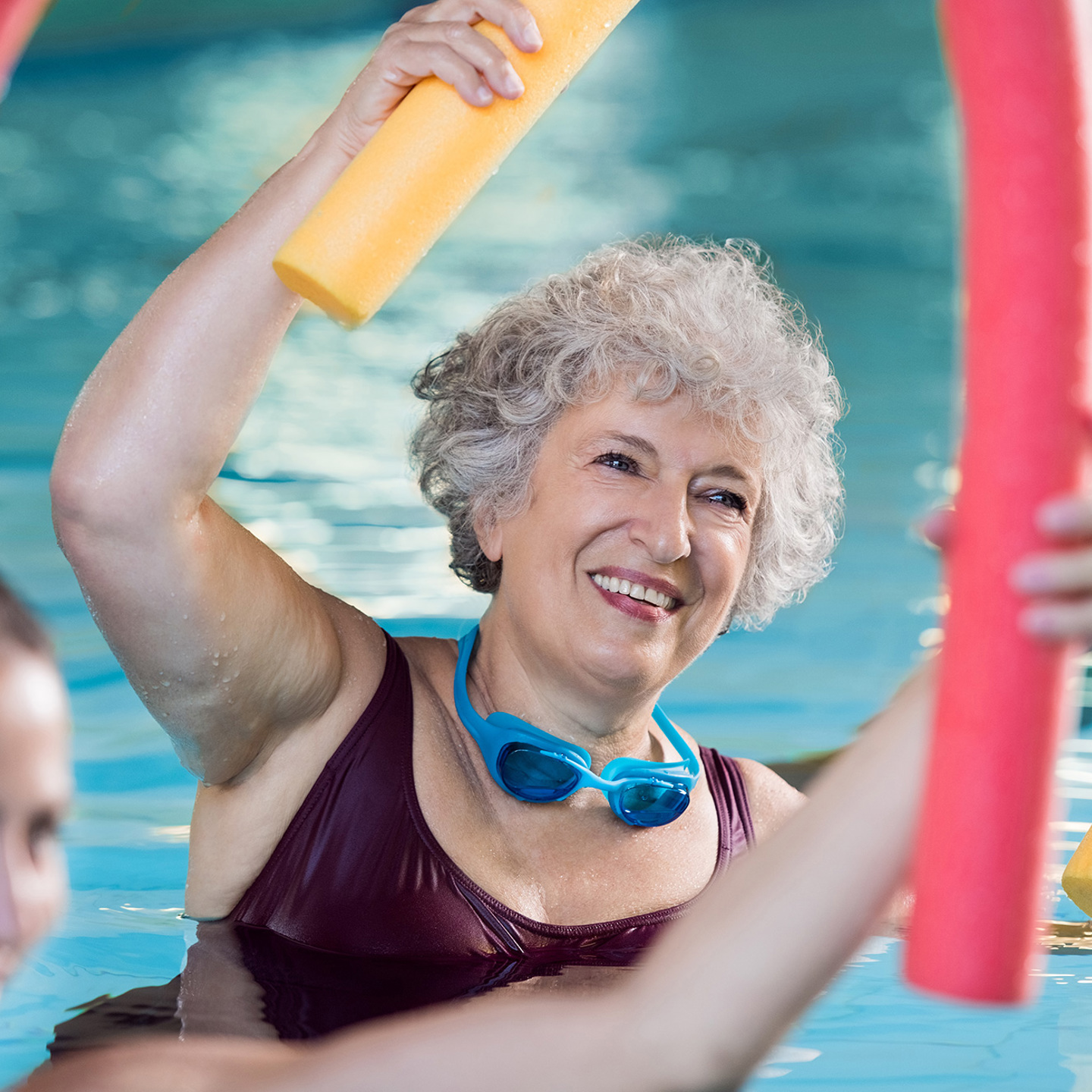 Woman exercising in a group fitness class taking place in the pool, the woman is smiling while following instructors instructions