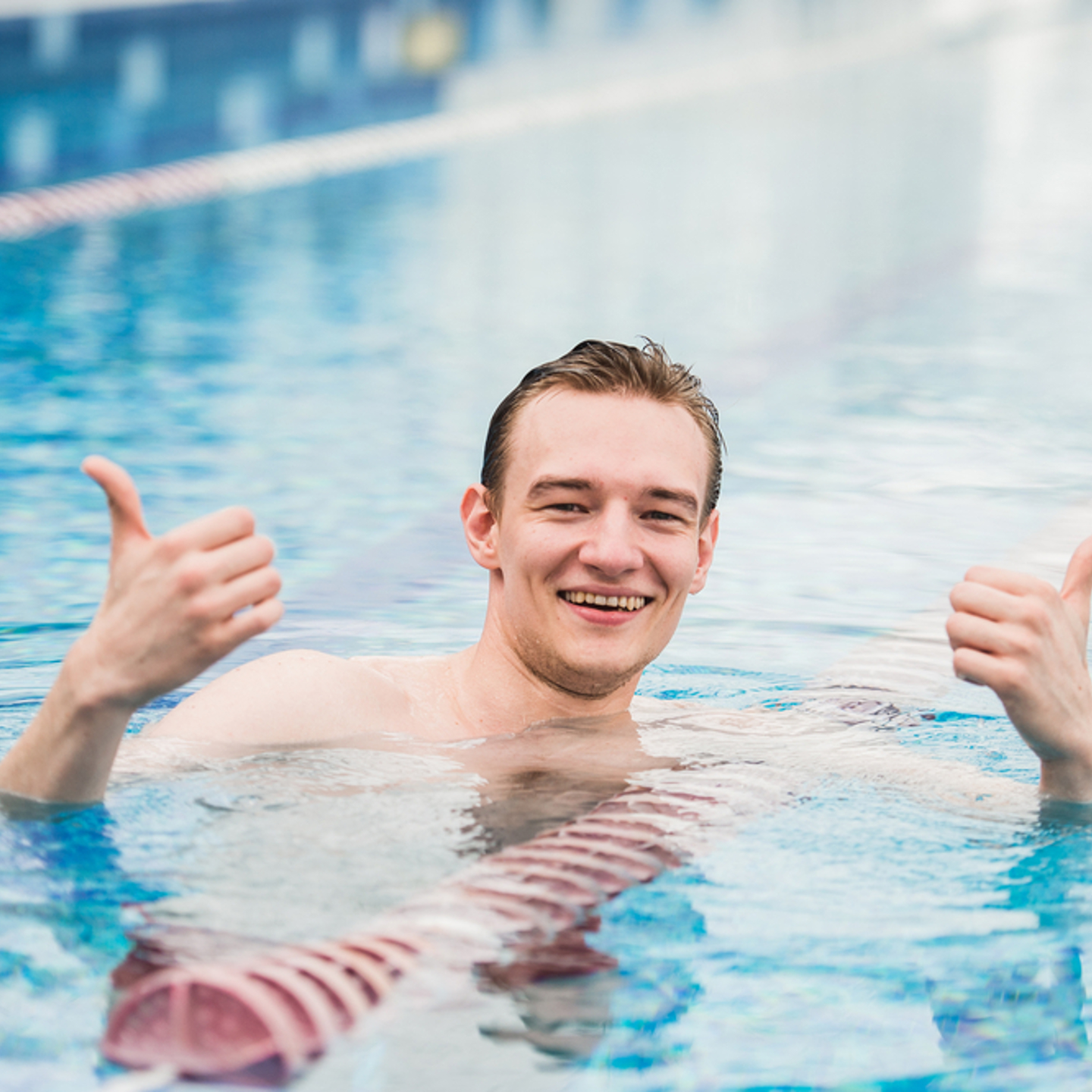 Person in a swimming pool, looking towards the camera and smiling while holding two thumbs up