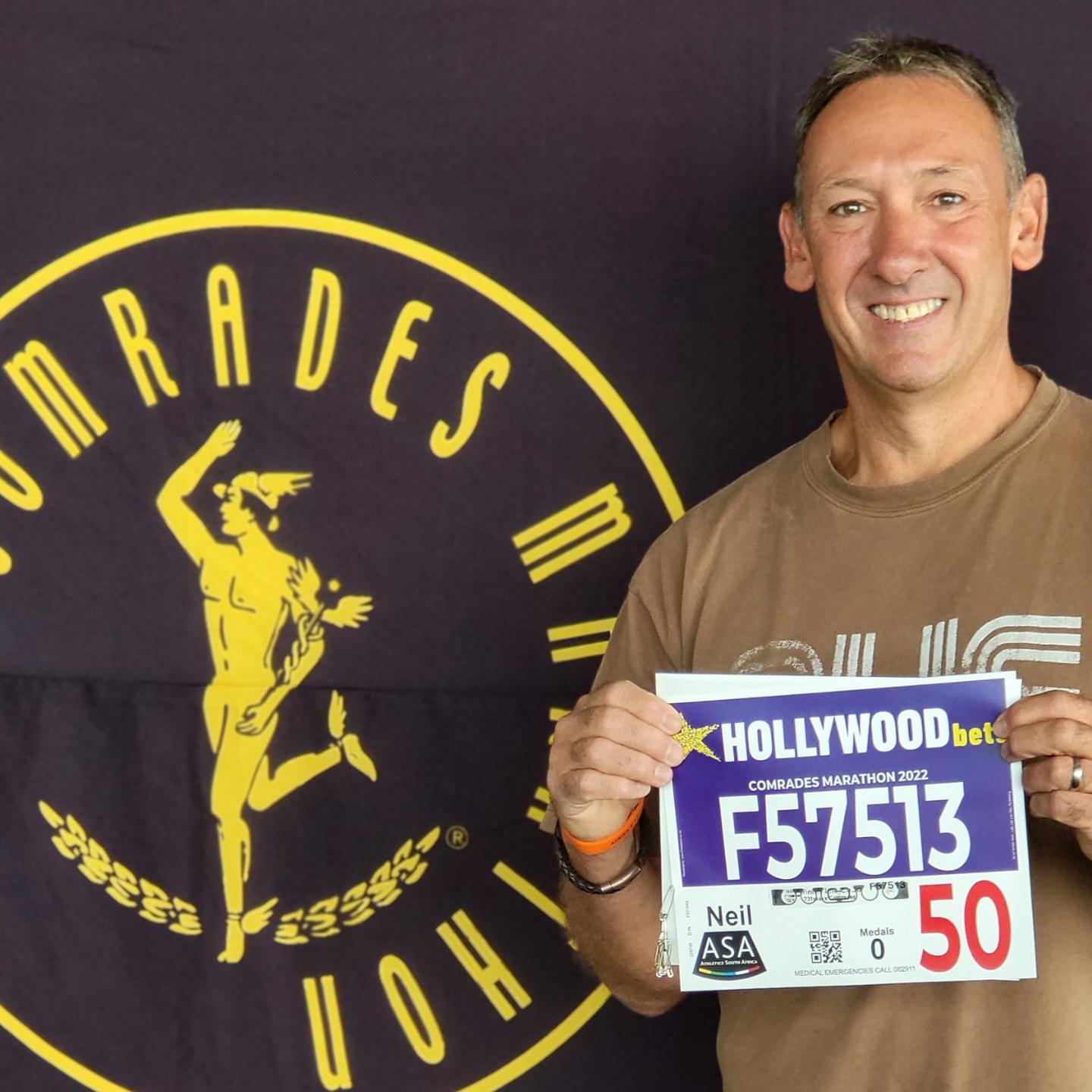 photo of Neil with his entry number for the Comrades Marathon in front of the Comrades logo