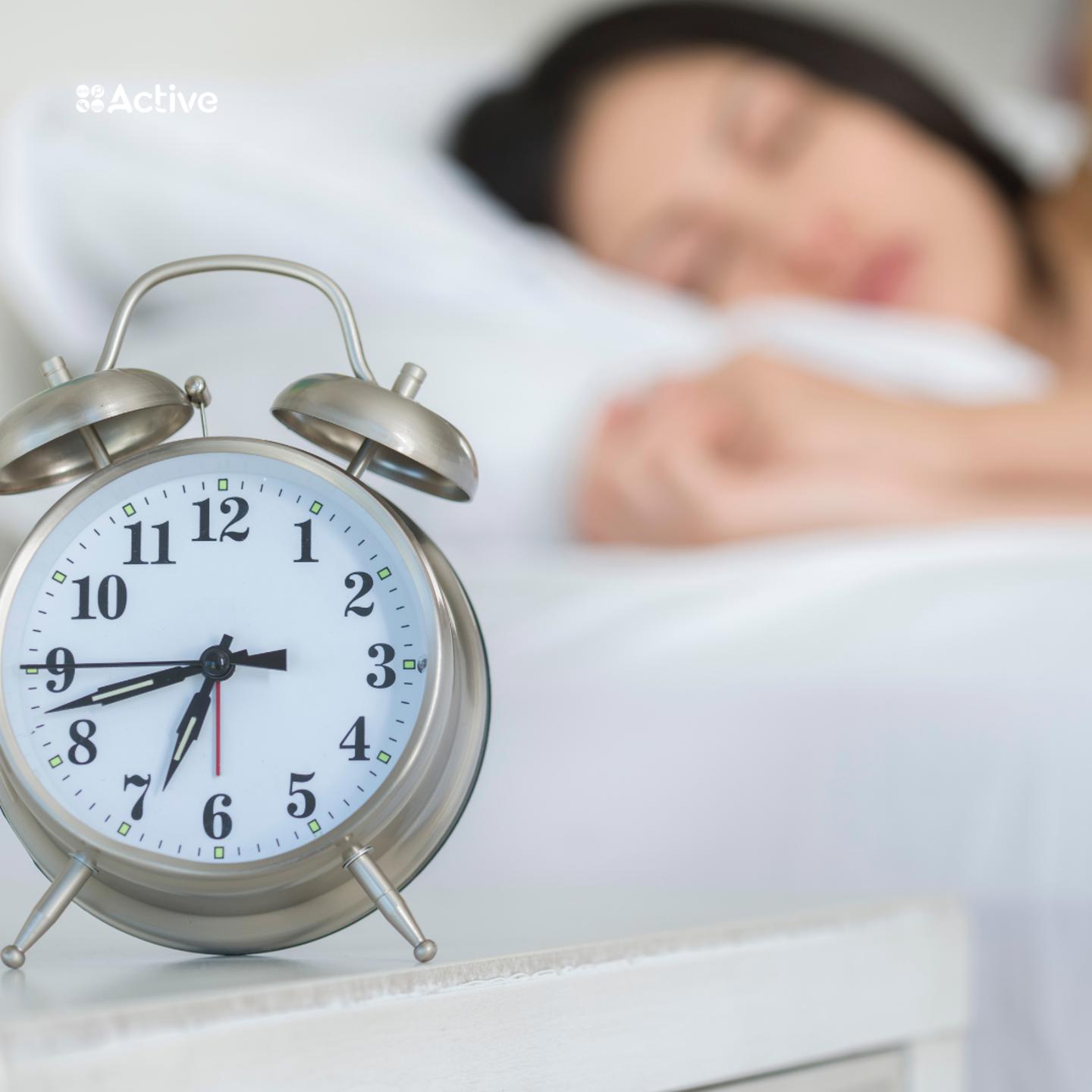 Photo of a close up of an alarm clock with a person in bed sleeping in the background