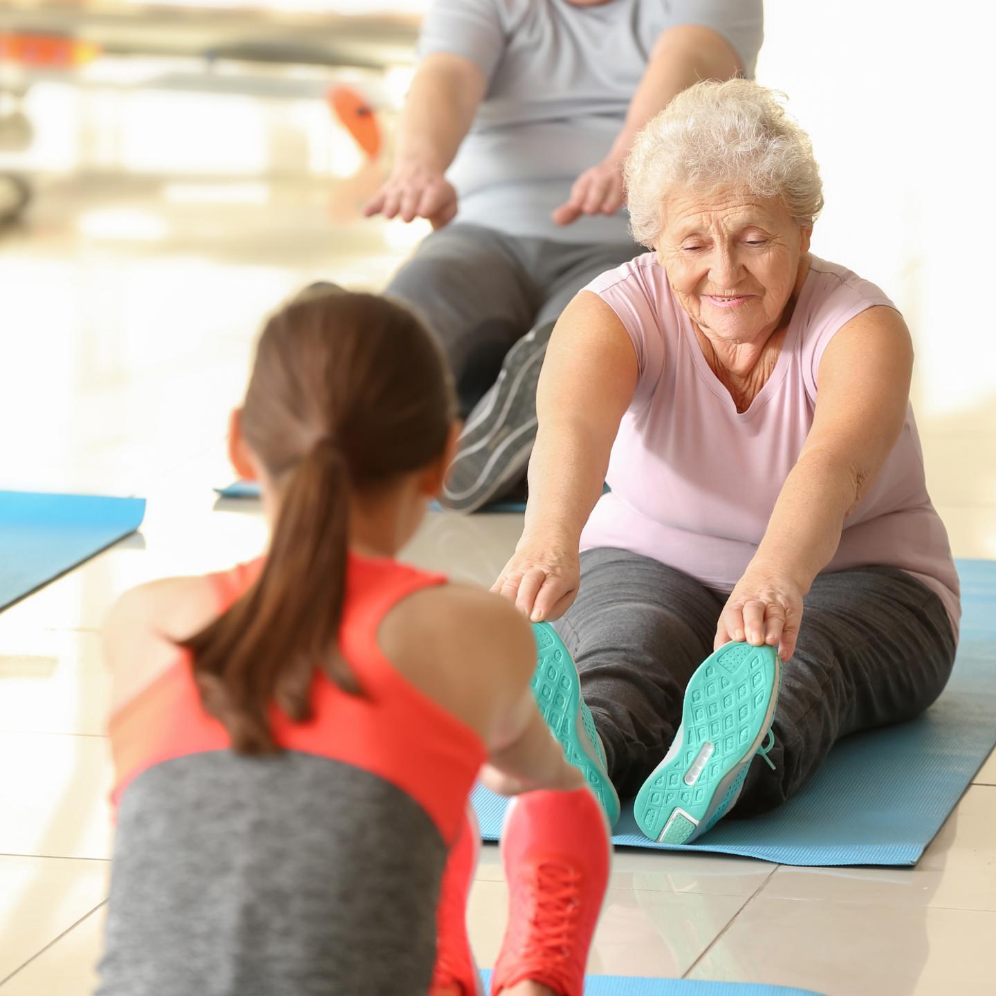 Photo of older person sat on a matt touching their feet in a stretching pose