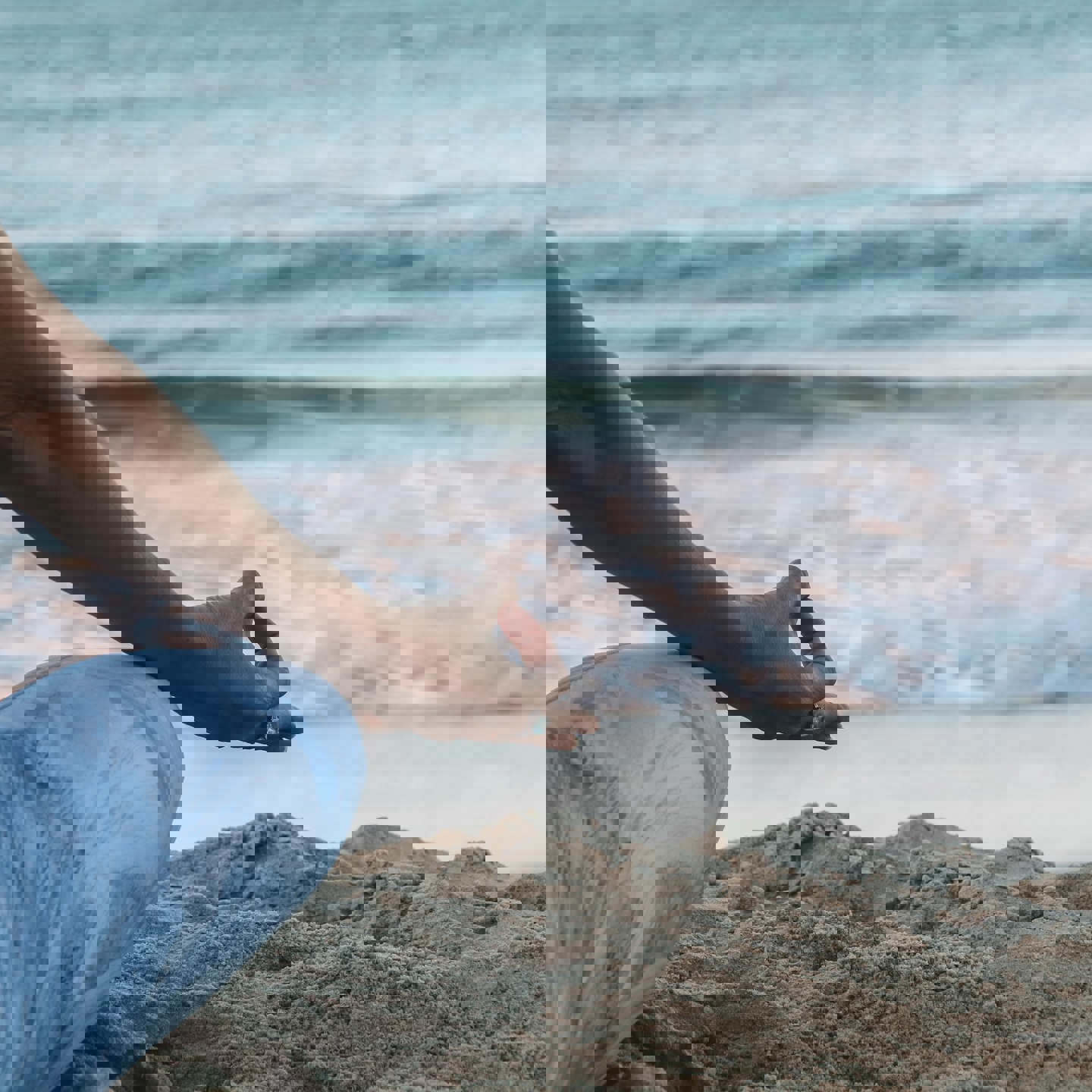 Image of a person sat on the sand on a beach looking towards the sea meditating