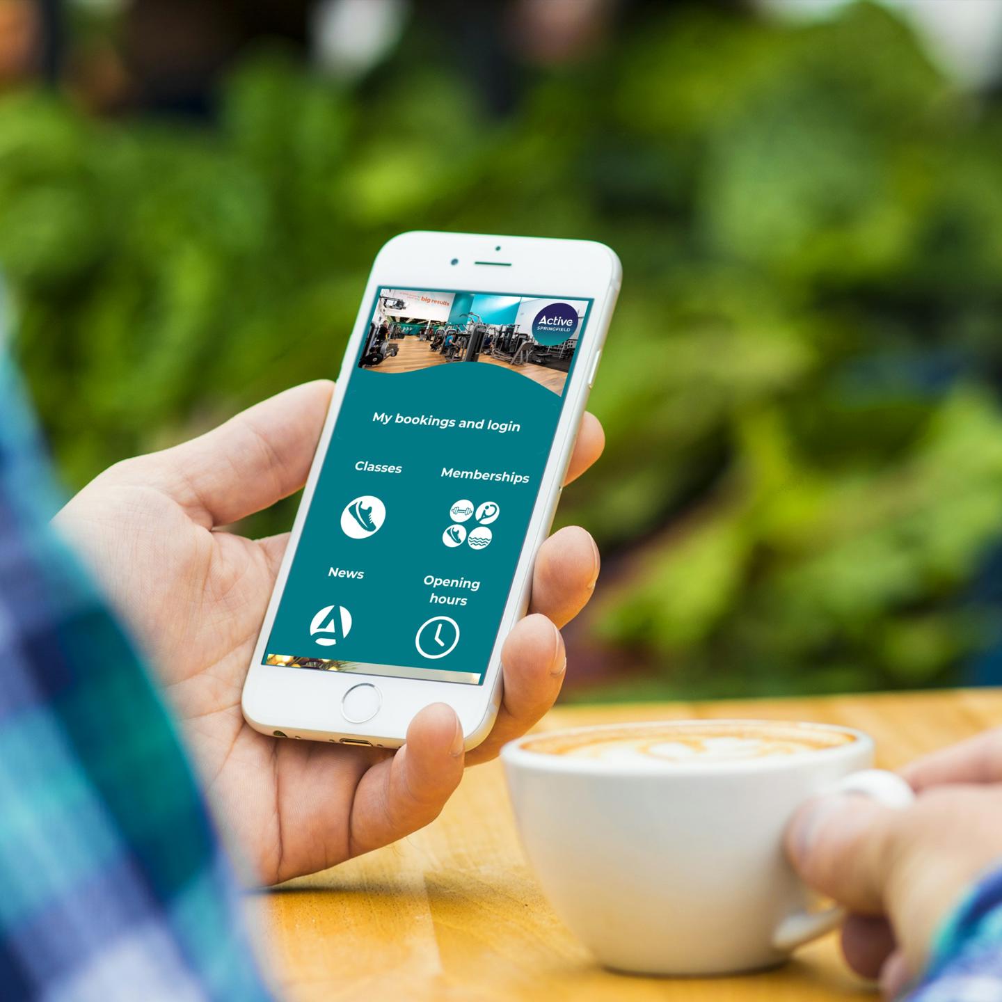 The Active Jersey App shown on an iPhone in a persons hand while they are drinking a coffee