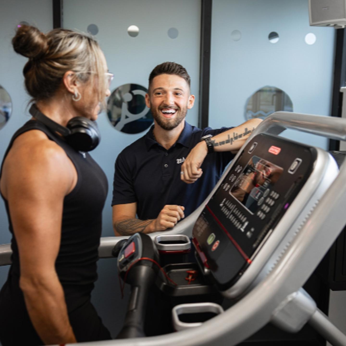 Photo of two people by a treadmill, one is being instructed by the other