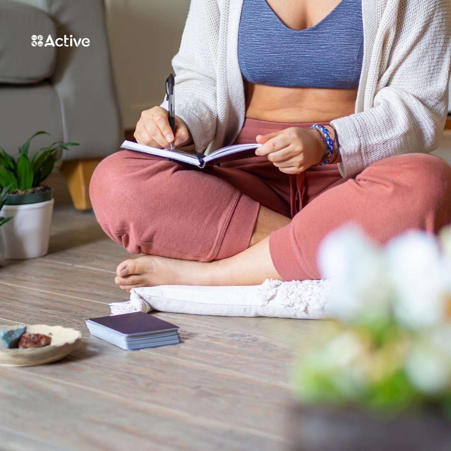 Photo of a person sat on the floor with their legs crossed while writing in a journal