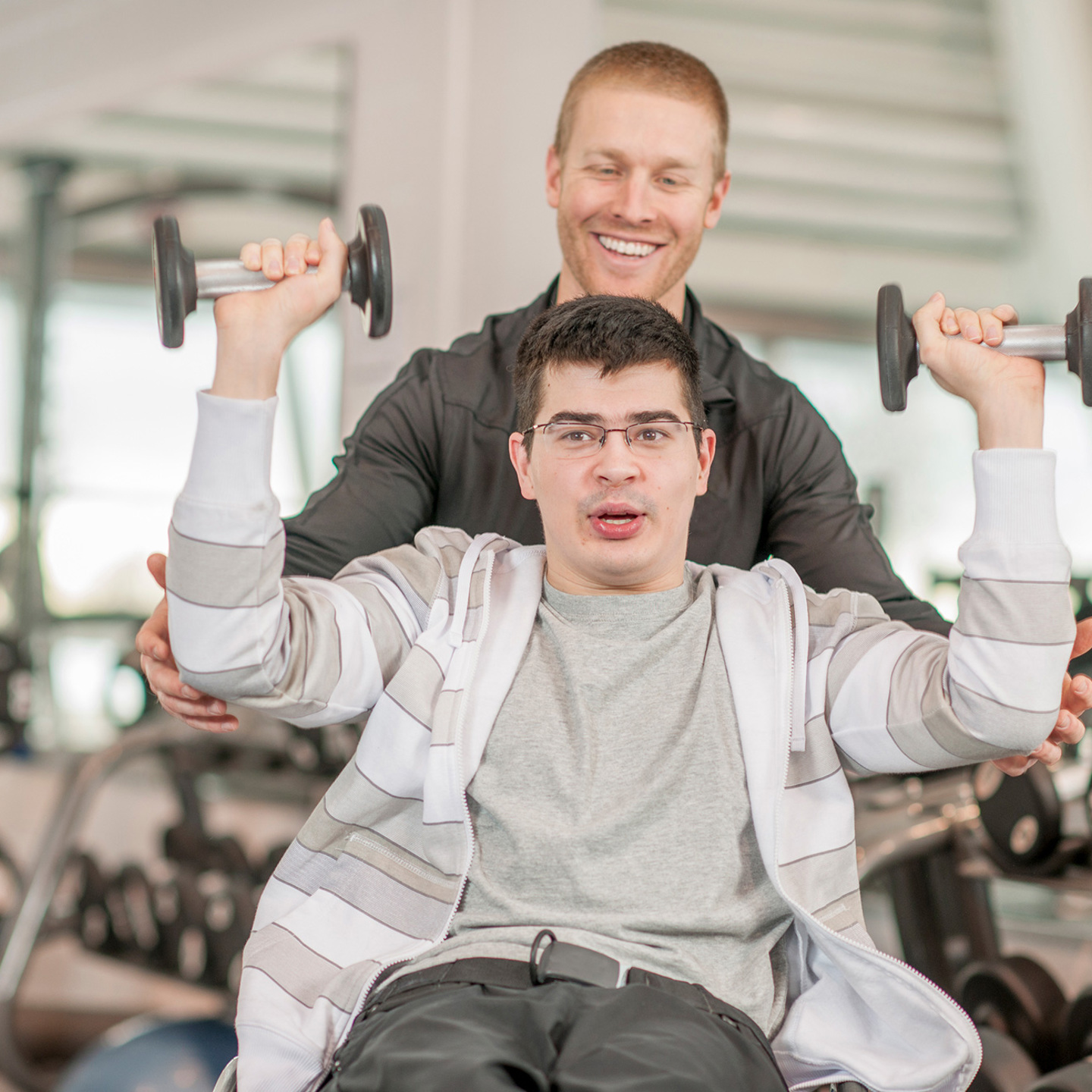 Photo of a person lifting some weights being helped by a staff member