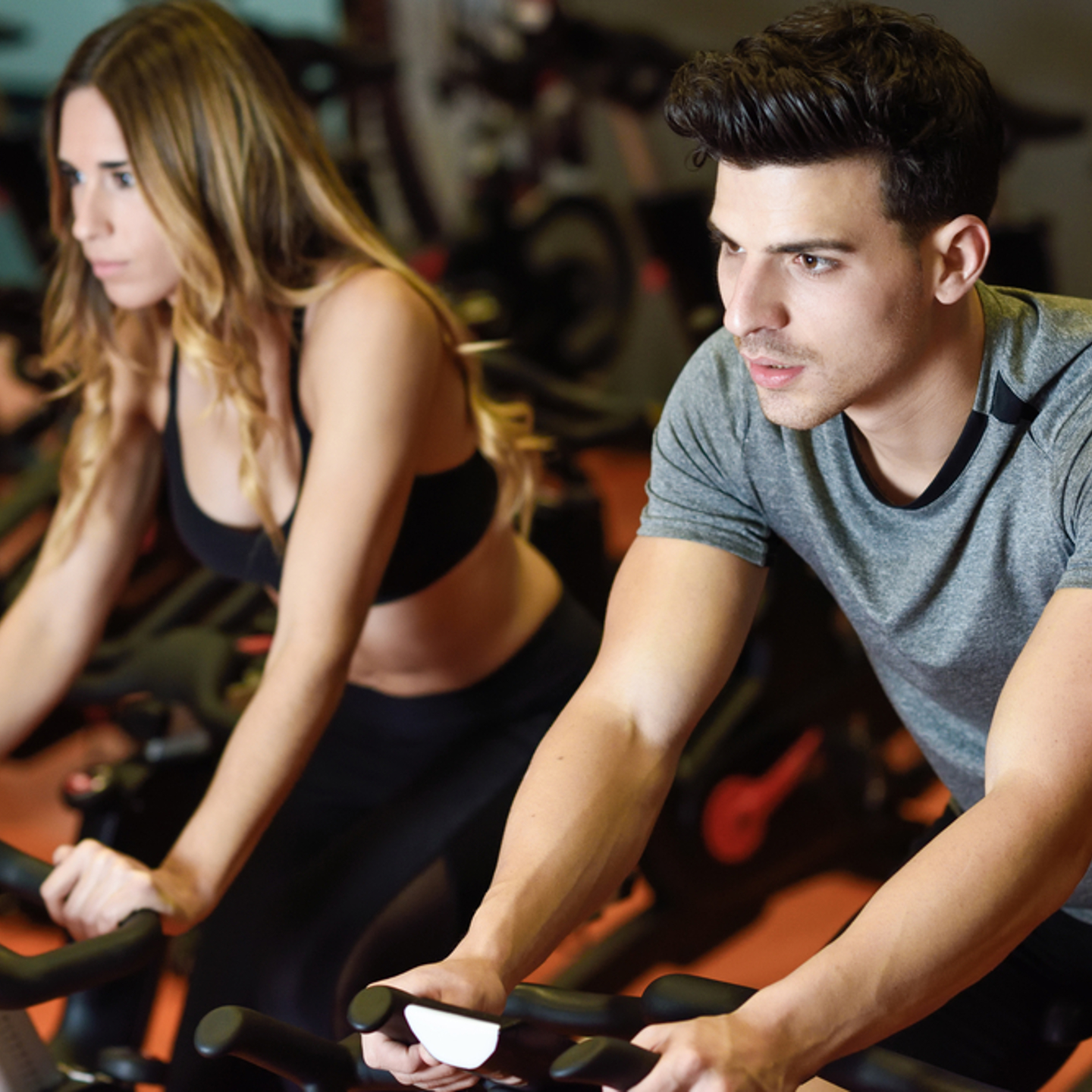 A woman and a man on spin bikes concentrating on their class