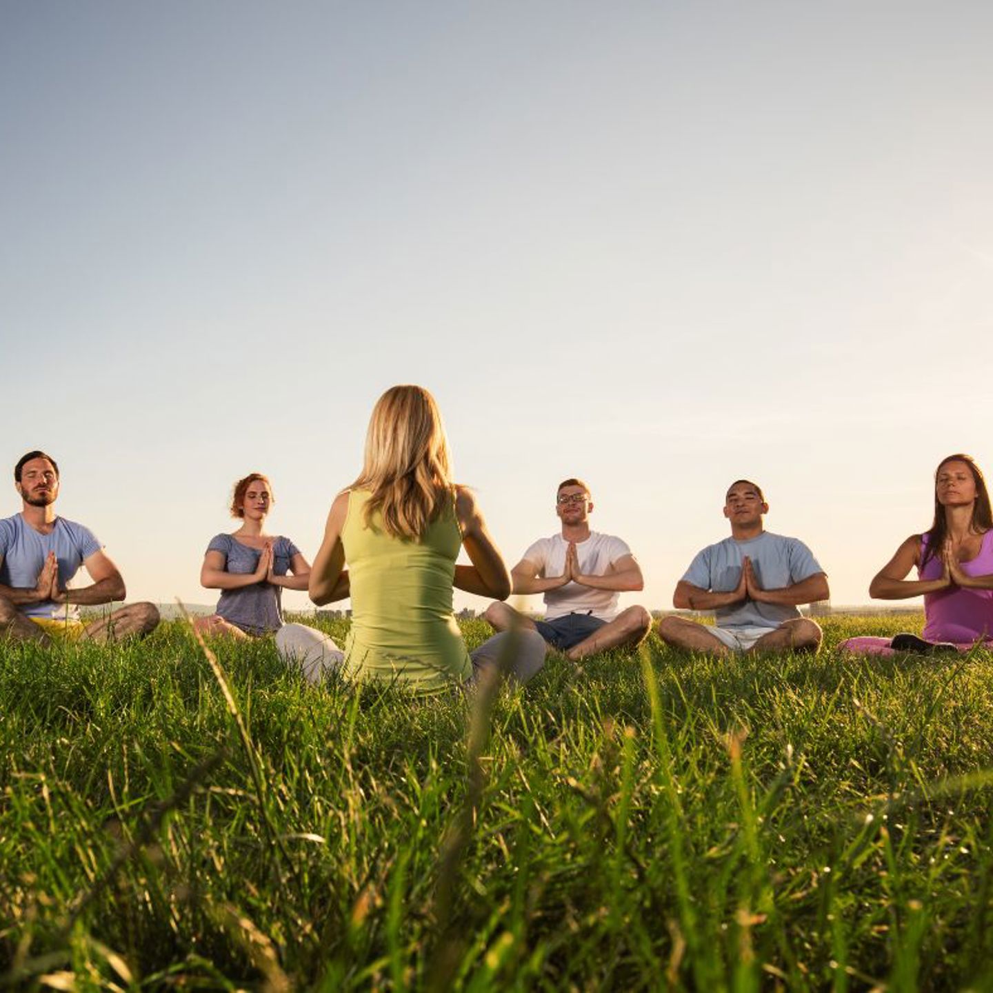 Photo of people taking part in a meditation practise in a field, the instructor has their back to the camera