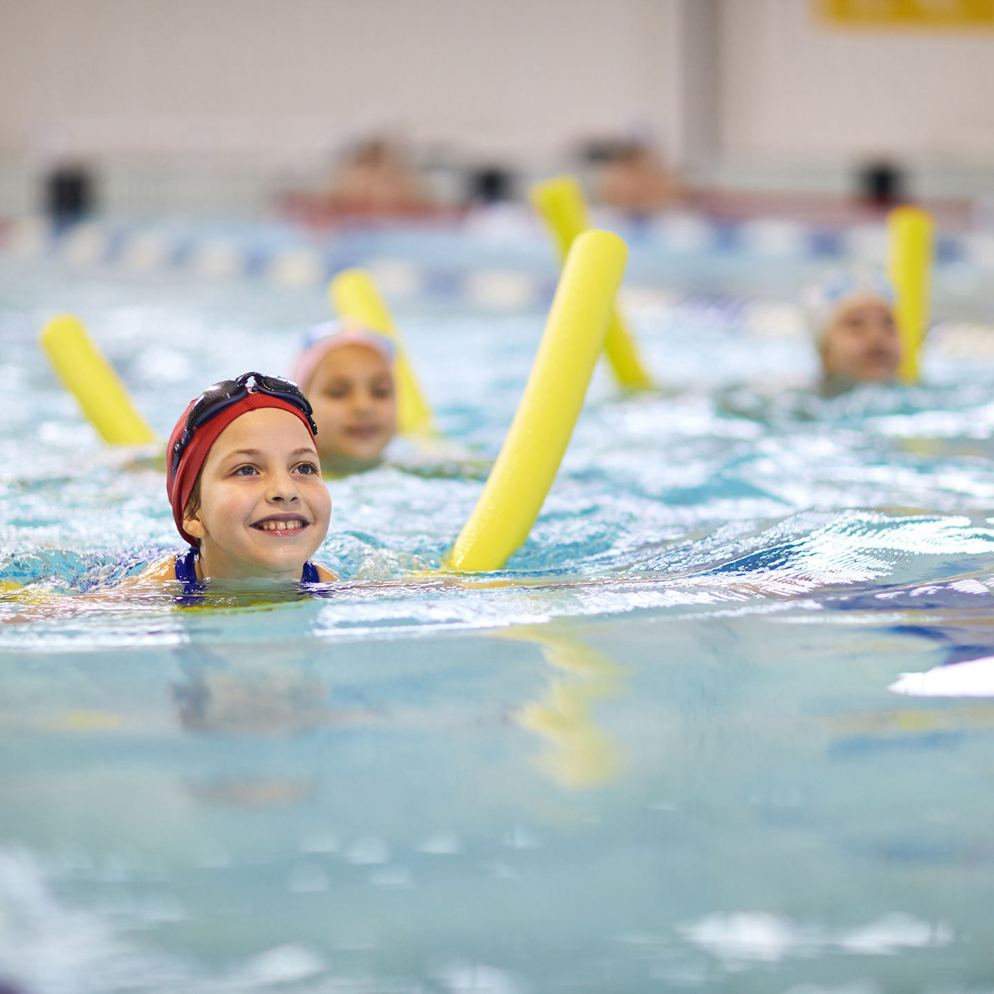smiling child swimming in the pool with a floatation device, two other children in the background