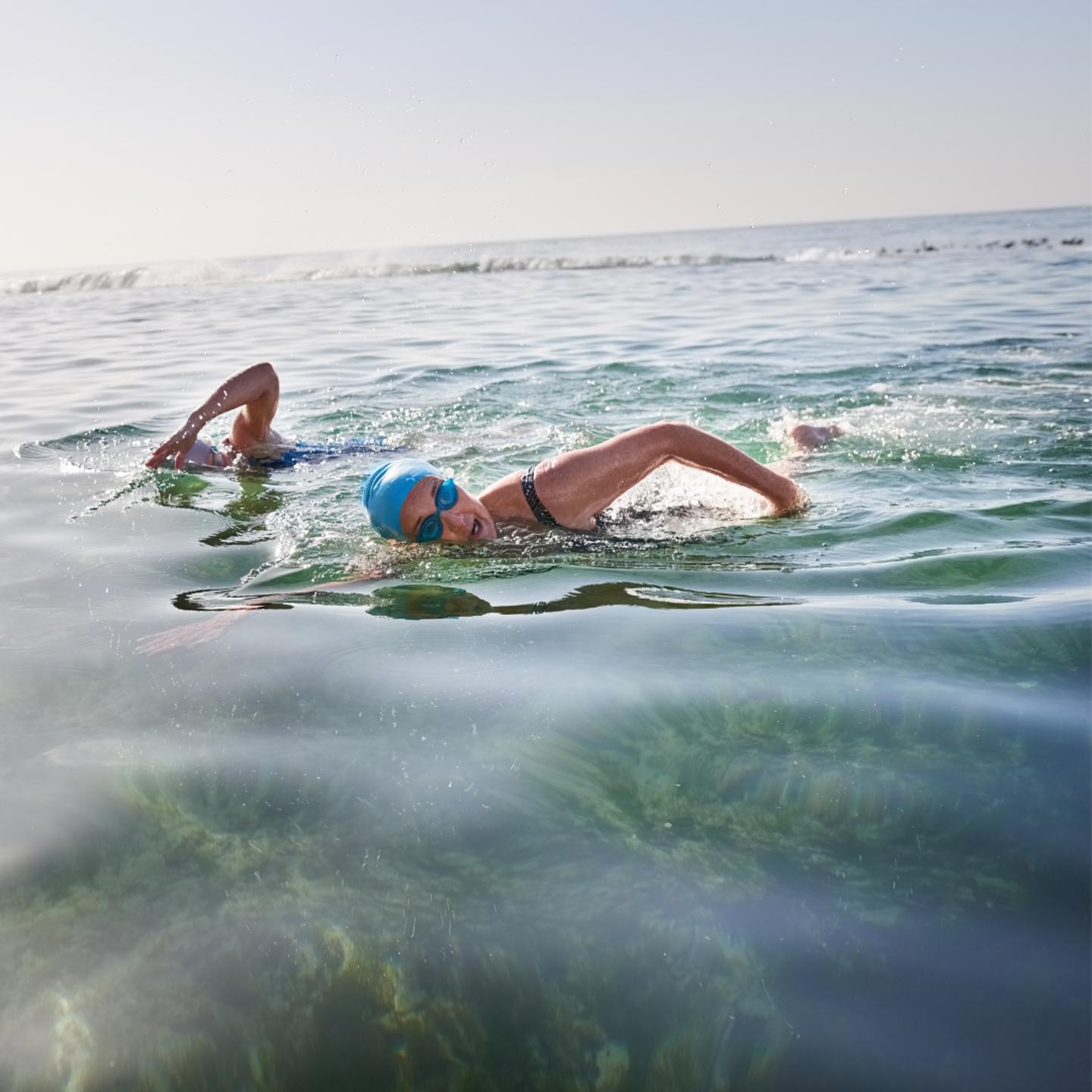 Photo of two people swimming outdoors in the sea, they are both wearing swimming goggles and hats