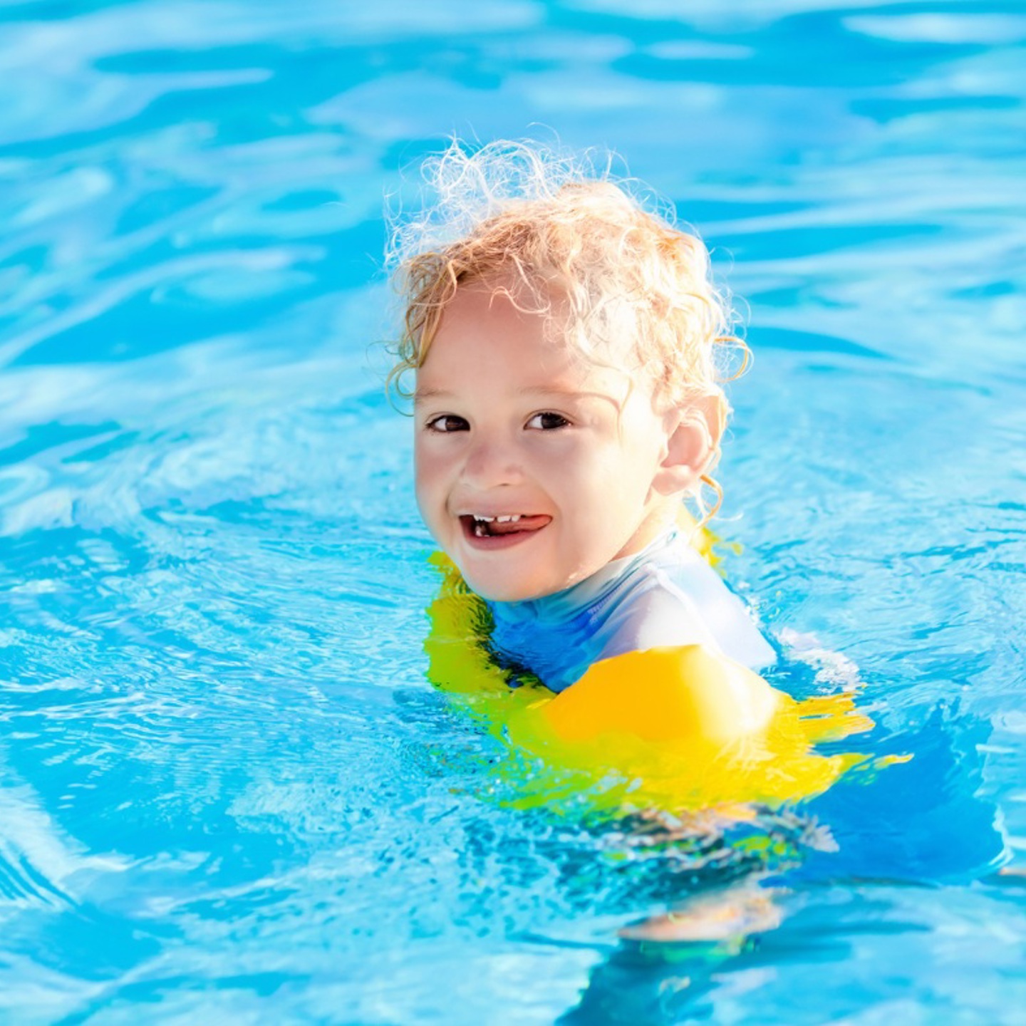 Small child in a swimming pool with yellow arm bands on, they are looking towards the camera and smiling