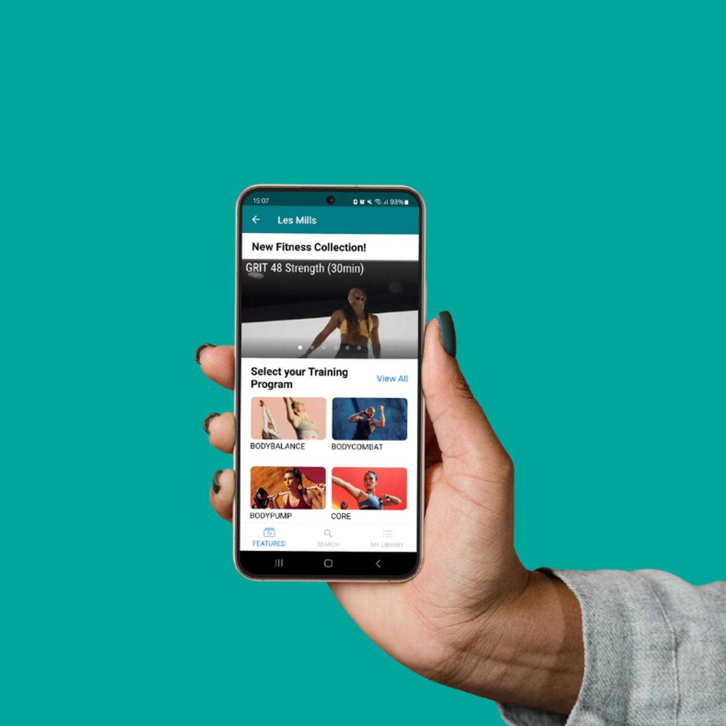 Android phone in a persons hand showing Les Mills On Demand, the picture has a turquoise background
