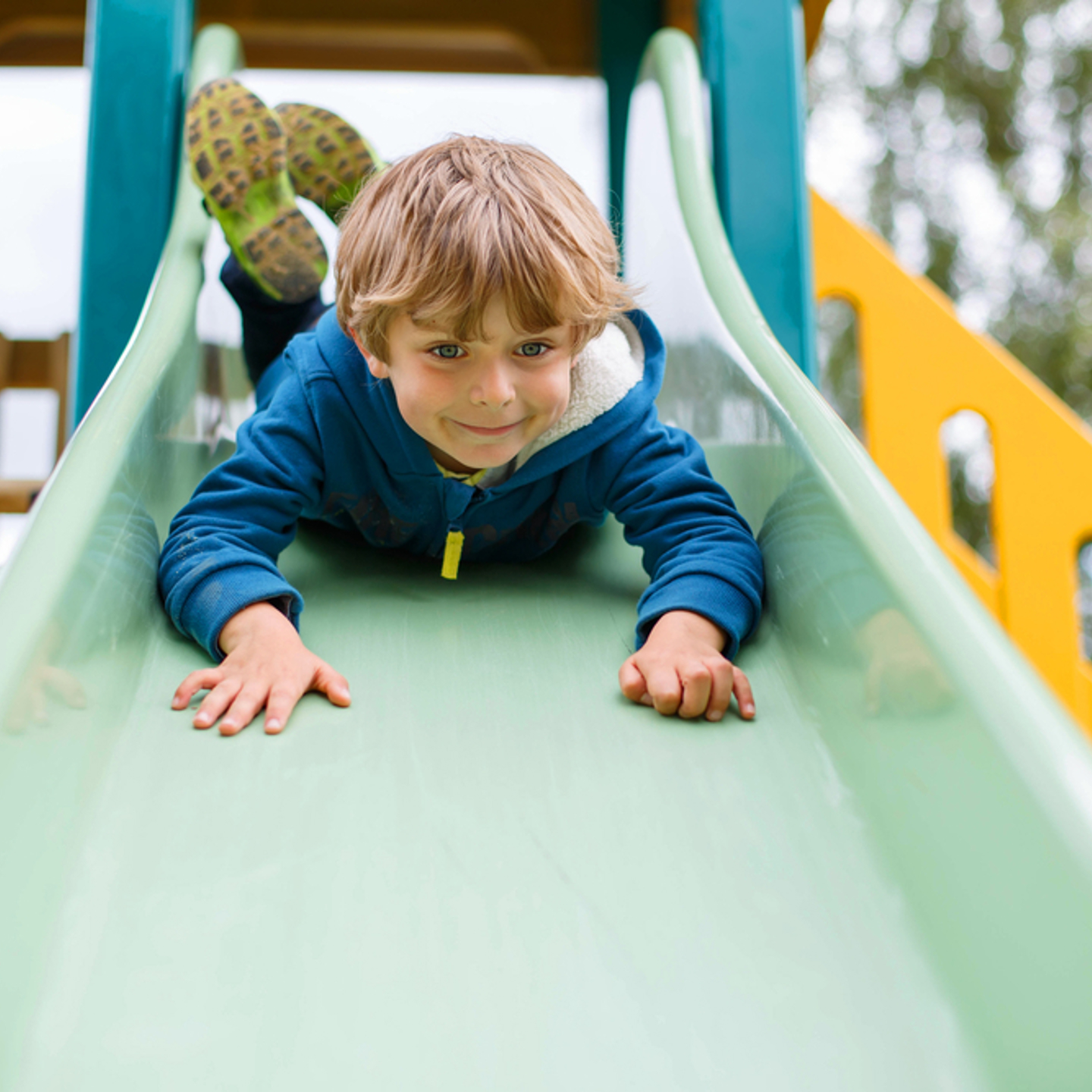 Child smiling while sliding down a slide in a play area
